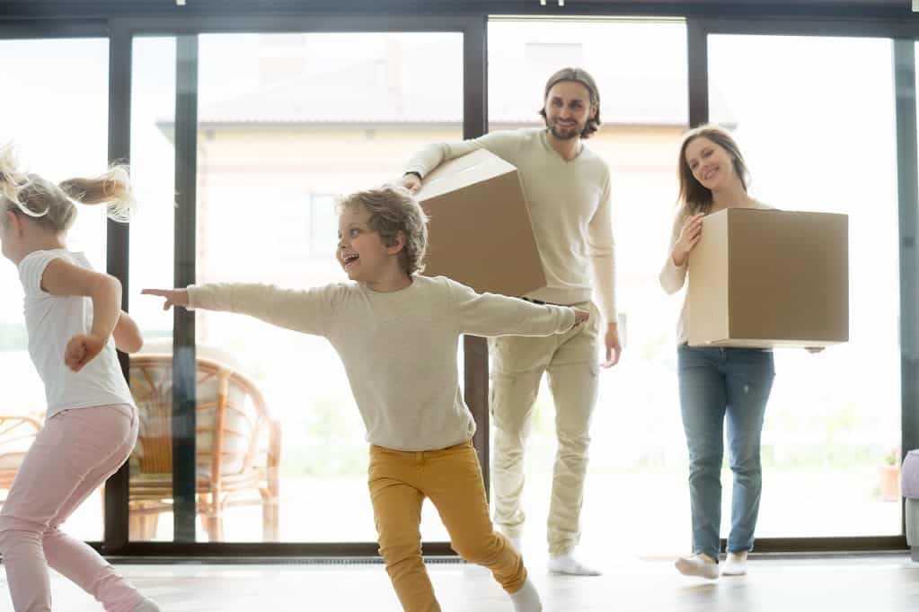 Kids playing in new home, parents holding boxes, moving day